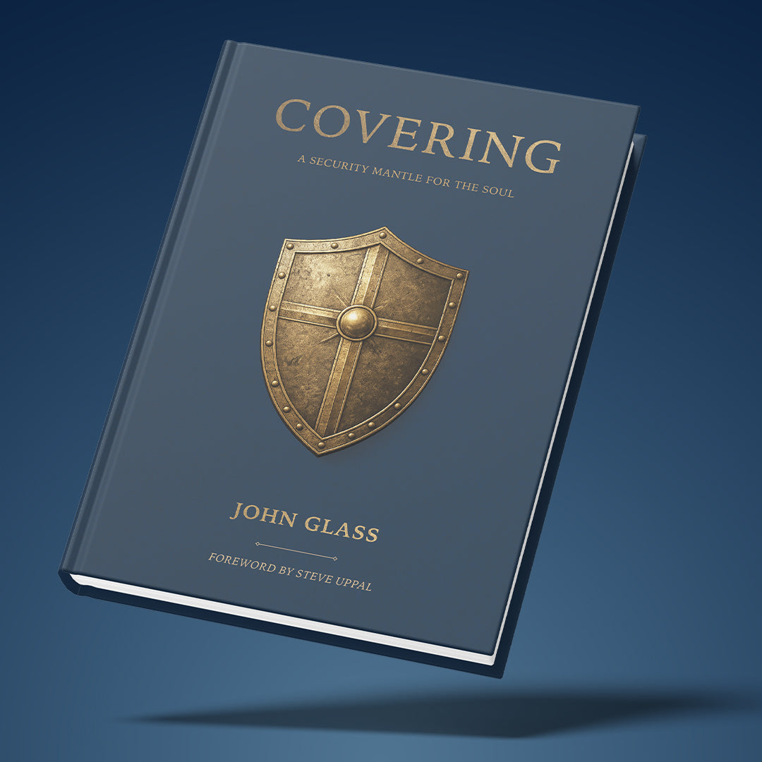 A hardcover book titled "Covering: A Security Mantle for the Soul" by John Glass, shown floating at an angle against a dark blue gradient background. The cover is slate blue with a metallic gold shield emblem in the center and gold lettering.