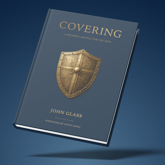 A hardcover book titled "Covering: A Security Mantle for the Soul" by John Glass, shown floating at an angle against a dark blue gradient background. The cover is slate blue with a metallic gold shield emblem in the center and gold lettering.